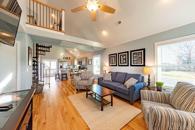 living area featuring high vaulted ceiling, visible vents, light wood-style flooring, and stairs