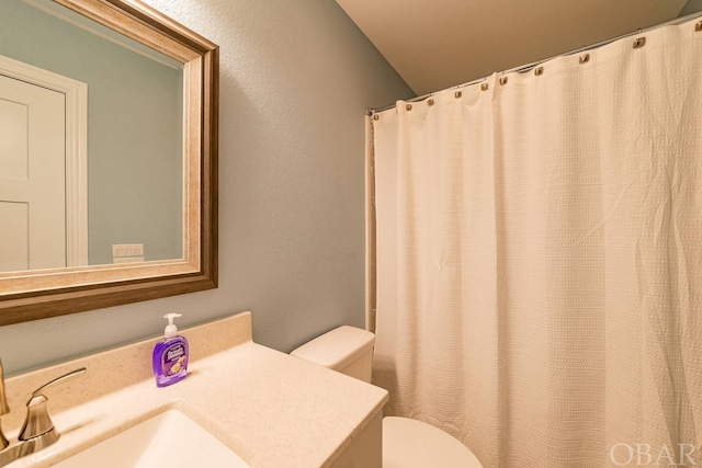 full bath featuring a textured wall, vanity, and toilet