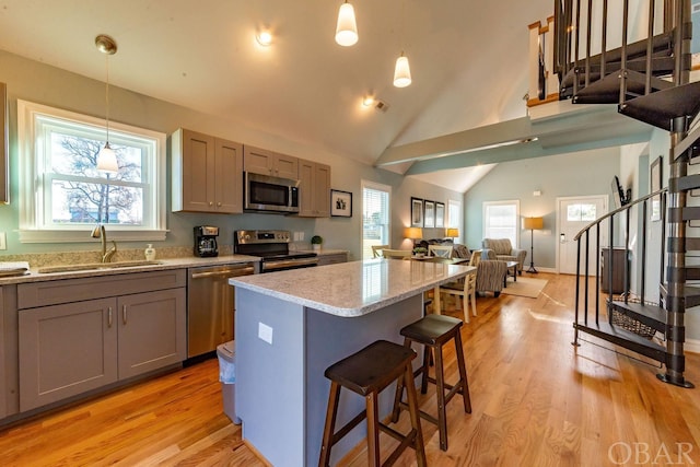 kitchen with stainless steel appliances, a sink, a healthy amount of sunlight, a kitchen breakfast bar, and decorative light fixtures