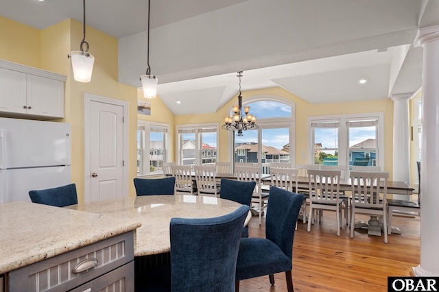 kitchen with decorative light fixtures, lofted ceiling, freestanding refrigerator, light stone countertops, and ornate columns