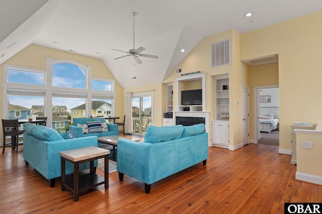 living room featuring high vaulted ceiling, built in shelves, a fireplace, wood finished floors, and visible vents