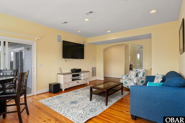 living room with light wood-style floors, arched walkways, visible vents, and recessed lighting