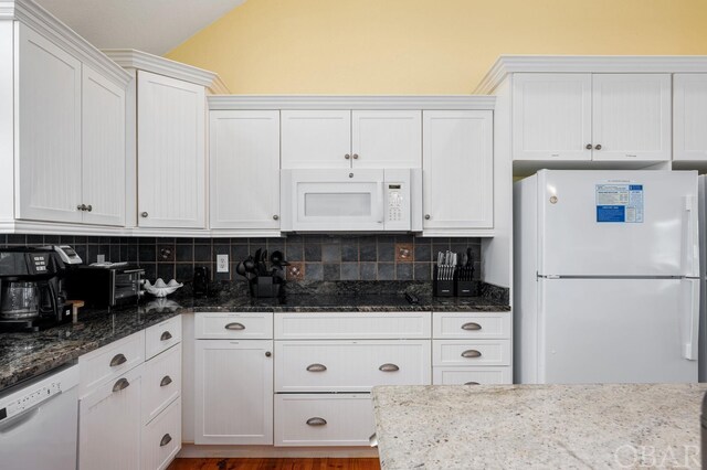 kitchen featuring white appliances, dark stone countertops, backsplash, and white cabinetry