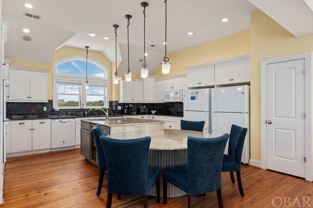 kitchen with light stone countertops, white appliances, a center island with sink, and white cabinetry