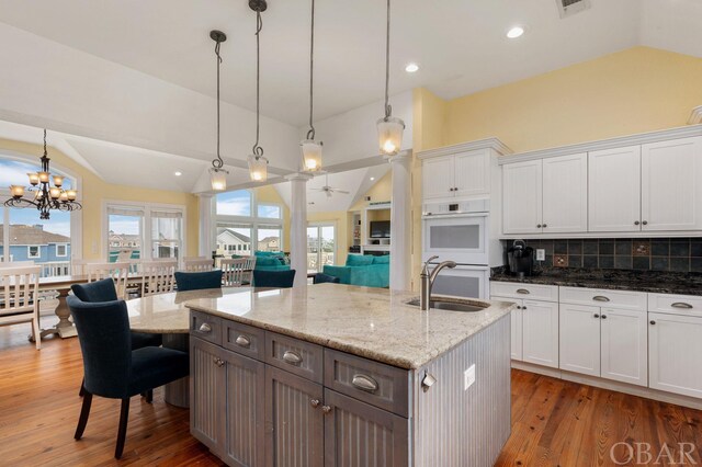 kitchen featuring an island with sink, double oven, white cabinets, and hanging light fixtures