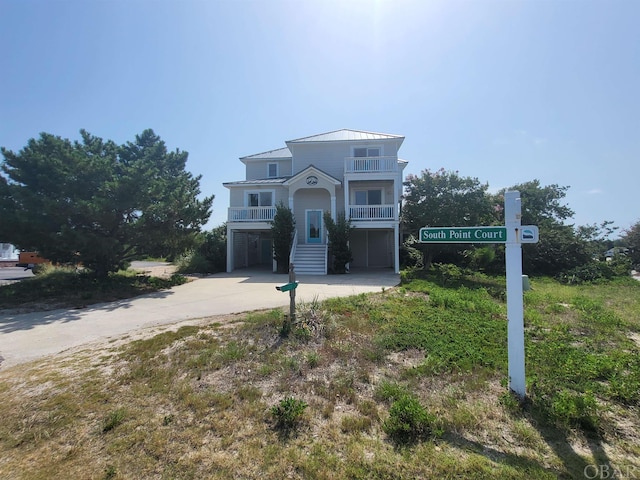 coastal inspired home with concrete driveway, a standing seam roof, metal roof, a balcony, and a carport