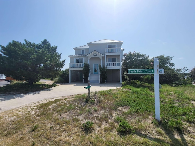 beach home featuring a balcony, concrete driveway, metal roof, a carport, and a standing seam roof