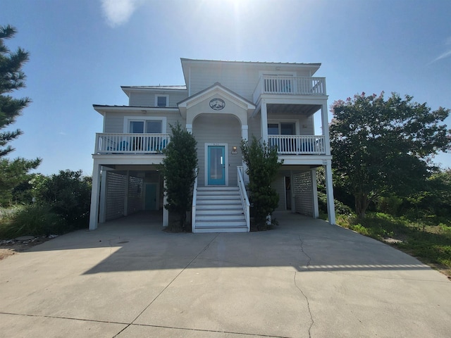 raised beach house featuring driveway, stairway, a carport, and a balcony