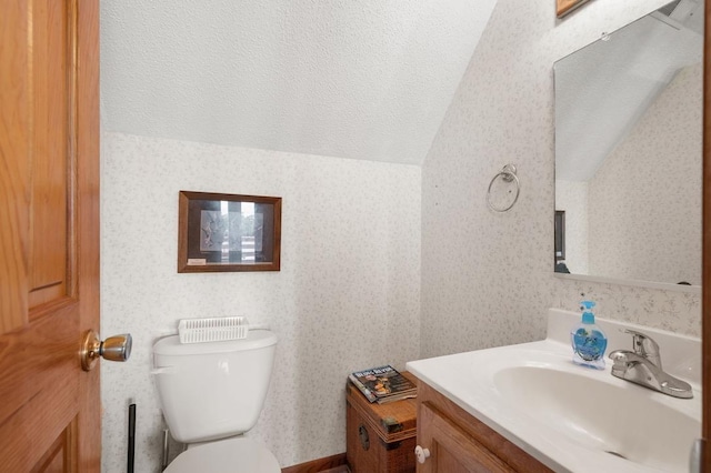 half bathroom with a textured ceiling, toilet, vanity, vaulted ceiling, and wallpapered walls