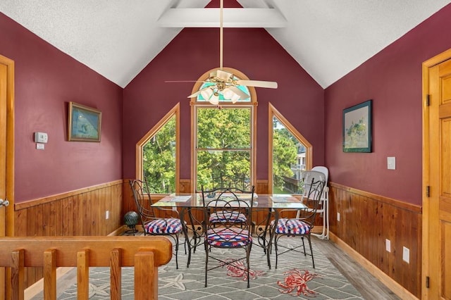 dining area with a wainscoted wall, wooden walls, lofted ceiling with beams, and wood finished floors