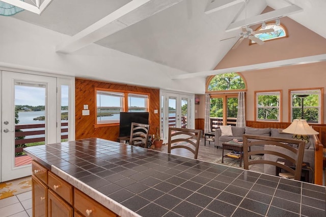 kitchen featuring tile countertops, a water view, a healthy amount of sunlight, french doors, and beam ceiling