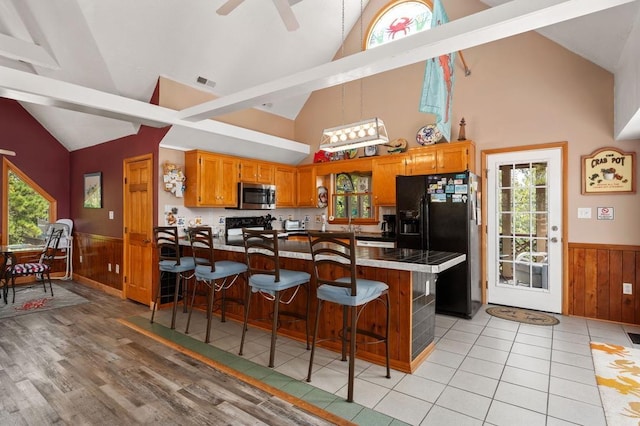 kitchen with a wainscoted wall, black fridge, stainless steel microwave, and a breakfast bar