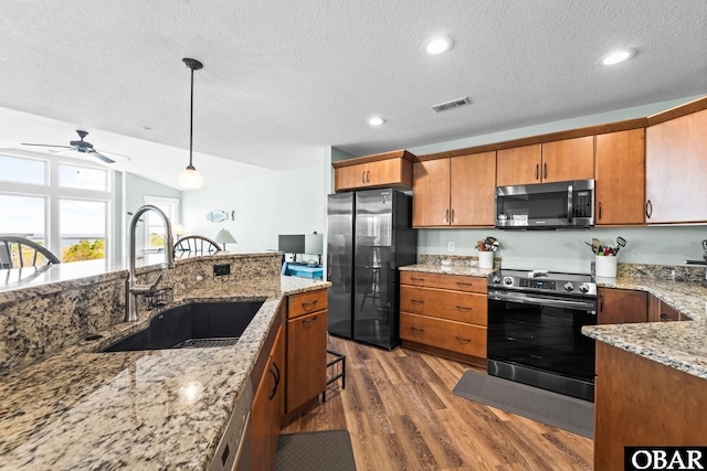 kitchen with pendant lighting, visible vents, appliances with stainless steel finishes, brown cabinetry, and a sink