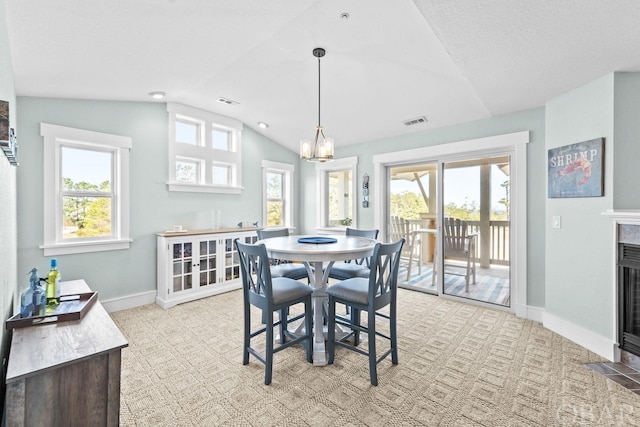 dining area with a fireplace with flush hearth, plenty of natural light, visible vents, and vaulted ceiling