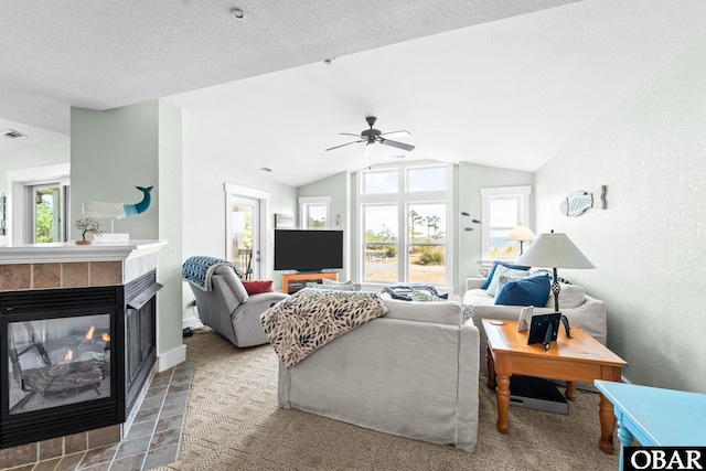 living area featuring vaulted ceiling, ceiling fan, a tiled fireplace, and a healthy amount of sunlight