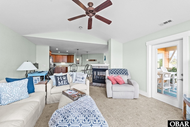 living area featuring ceiling fan, light colored carpet, a fireplace, visible vents, and vaulted ceiling