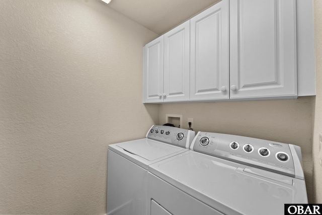 laundry room featuring cabinet space, a textured wall, and separate washer and dryer