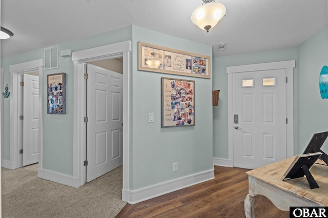 foyer entrance featuring baseboards, a textured ceiling, visible vents, and dark wood-type flooring