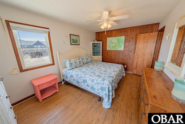 24143 Ocean Dr Lot 4, Rodanthe, NC 27968 - bedroom featuring light wood-style floors, a textured ceiling, wood walls, baseboards, and a ceiling fan