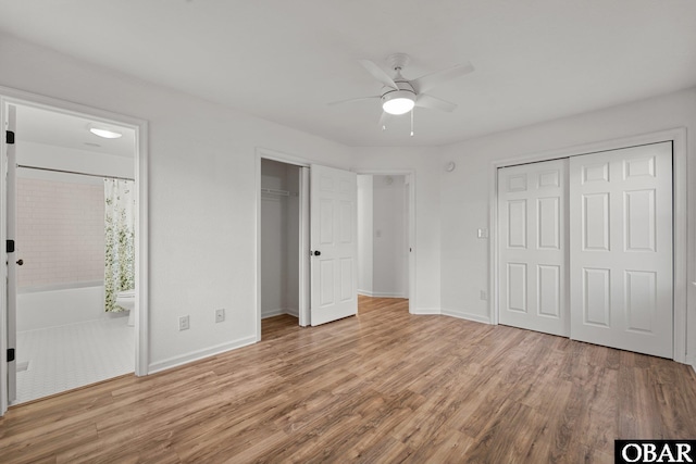 unfurnished bedroom with ensuite bathroom, a ceiling fan, baseboards, multiple closets, and light wood finished floors