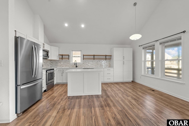 kitchen with white cabinets, wood finished floors, hanging light fixtures, stainless steel appliances, and light countertops