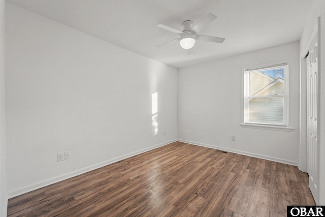 spare room featuring dark wood-style floors, a ceiling fan, and baseboards