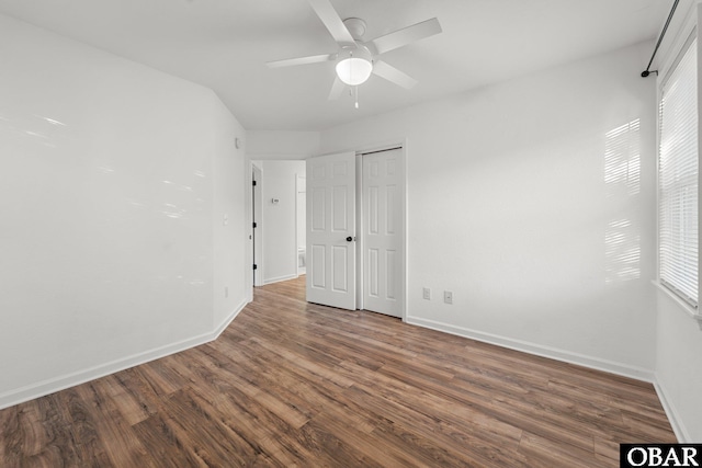 unfurnished bedroom with a ceiling fan, multiple windows, baseboards, and dark wood-type flooring