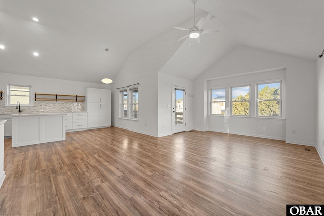 unfurnished living room with high vaulted ceiling, light wood-type flooring, ceiling fan, and baseboards