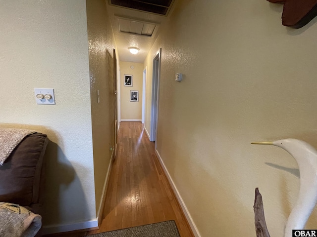 hallway with wood-type flooring, baseboards, attic access, and visible vents