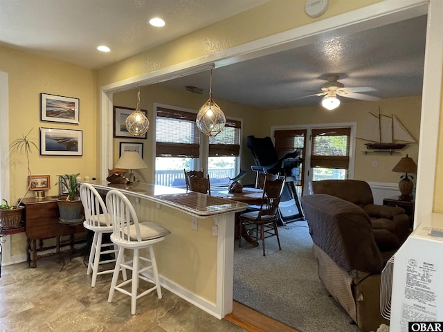kitchen with a kitchen bar, a peninsula, ceiling fan, and plenty of natural light