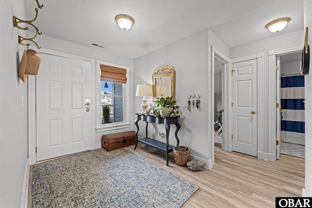 foyer entrance with baseboards, wood finished floors, and visible vents