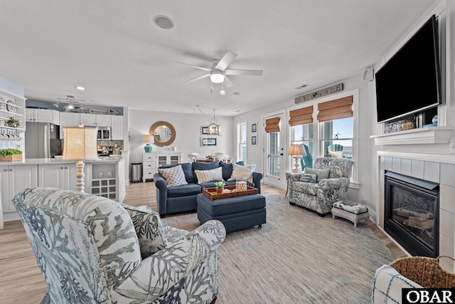 living area with a tiled fireplace, ceiling fan, light wood finished floors, and visible vents