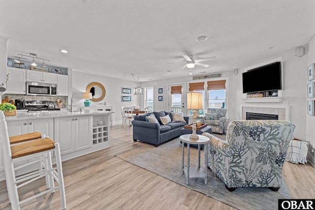 living area featuring light wood-style floors, baseboards, ceiling fan, recessed lighting, and a tiled fireplace