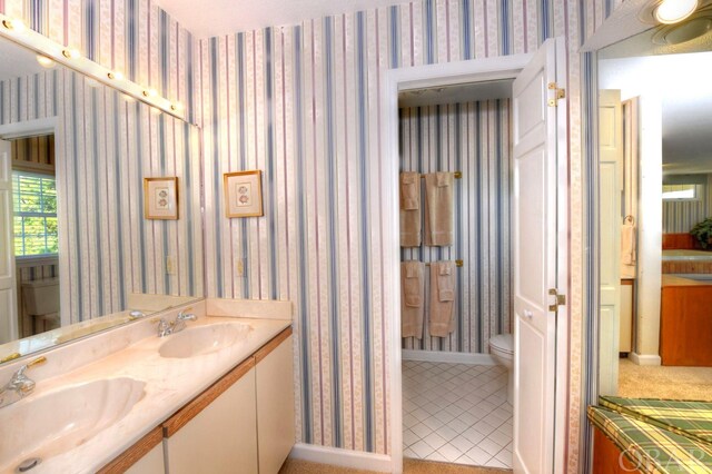 full bathroom with double vanity, a sink, toilet, and wallpapered walls