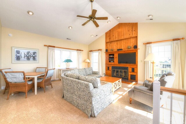 living area with a ceiling fan, a glass covered fireplace, light colored carpet, and high vaulted ceiling