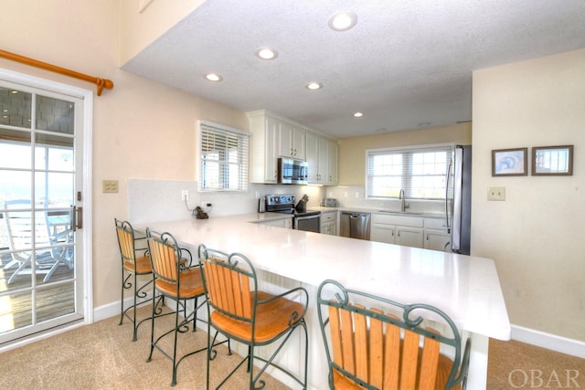 kitchen with a peninsula, stainless steel appliances, light countertops, and light colored carpet