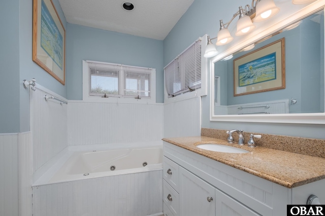 bathroom with a tub with jets, wainscoting, and vanity