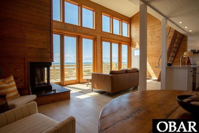 living area featuring a multi sided fireplace, a high ceiling, light wood-style flooring, wood walls, and recessed lighting
