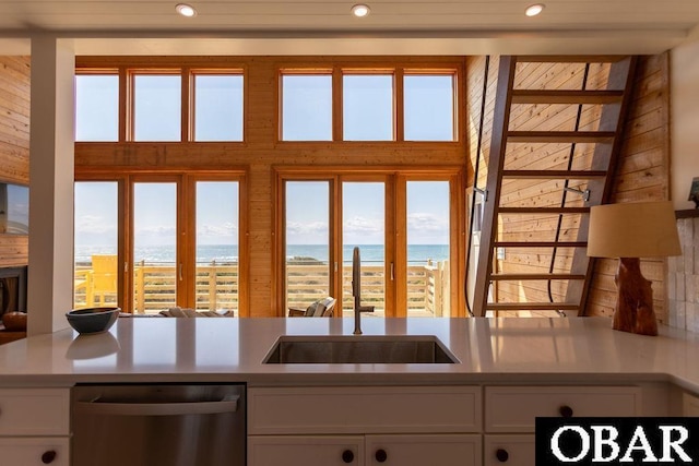 kitchen with stainless steel dishwasher, a sink, a water view, recessed lighting, and white cabinetry