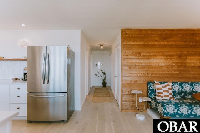 kitchen featuring light wood-type flooring, wooden walls, freestanding refrigerator, white cabinetry, and light countertops