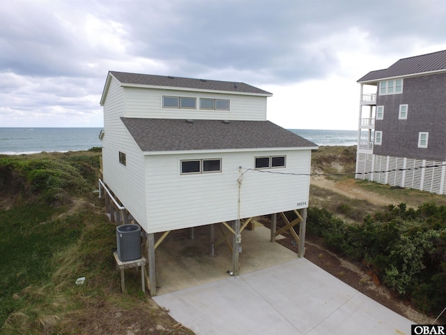 rear view of house featuring concrete driveway, a water view, a carport, cooling unit, and roof with shingles