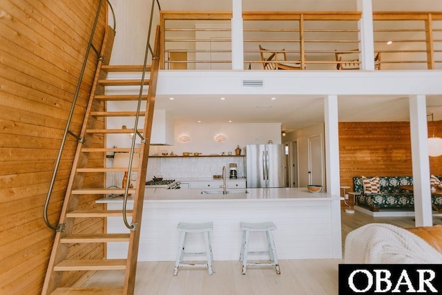kitchen with a sink, visible vents, freestanding refrigerator, wood finished floors, and wooden walls