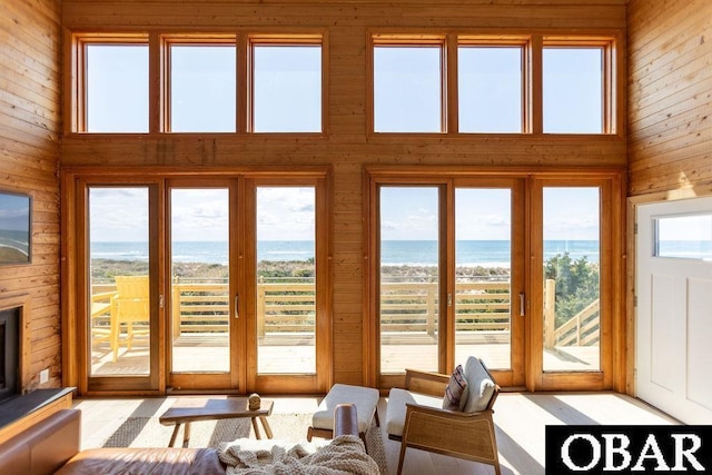 living area featuring a wealth of natural light, a towering ceiling, wooden walls, and a water view