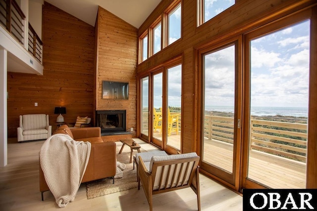 living room with wood walls, high vaulted ceiling, a water view, light wood-style floors, and a large fireplace