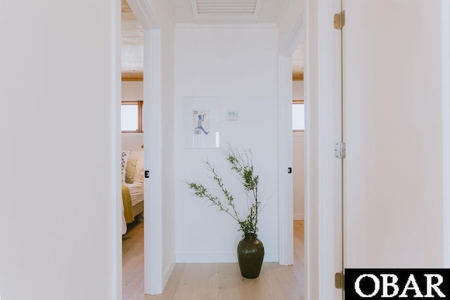 hall with light wood finished floors, baseboards, visible vents, and ornamental molding