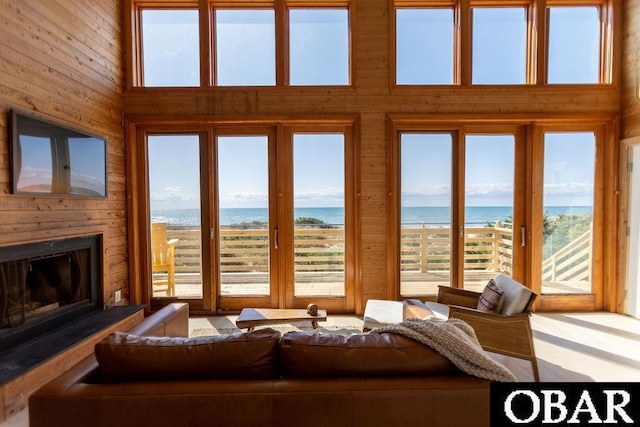 living room featuring plenty of natural light, wood walls, a large fireplace, and a water view
