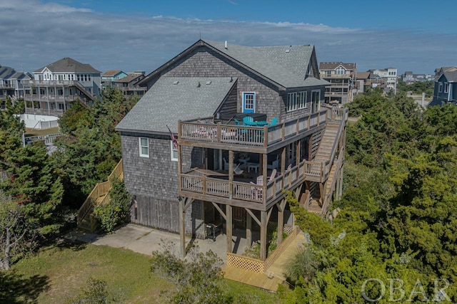 rear view of house featuring a deck, a patio, a balcony, a shingled roof, and stairs