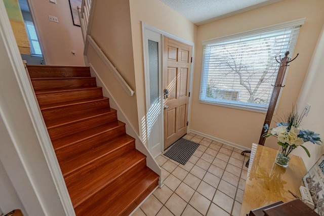 foyer with light tile patterned floors, baseboards, stairway, and a textured ceiling