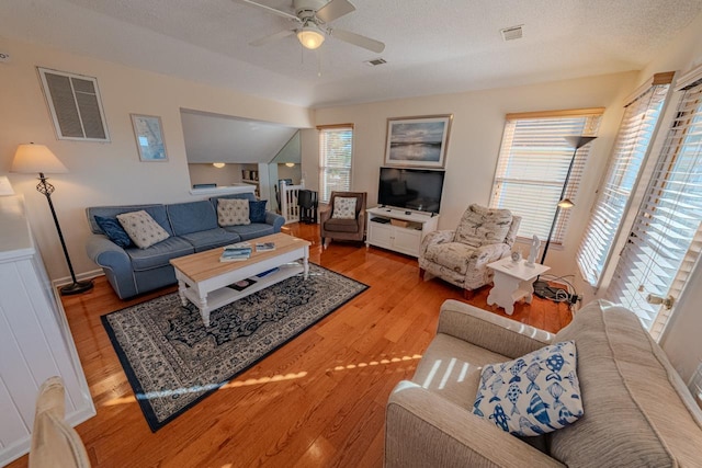 living area featuring light wood finished floors, a ceiling fan, visible vents, and a textured ceiling