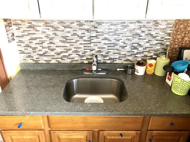 details with decorative backsplash, dark stone counters, sink, and white cabinetry